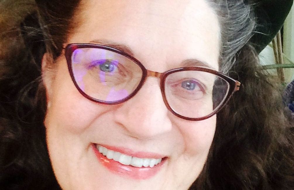 A woman in glasses smiles for the camera.
