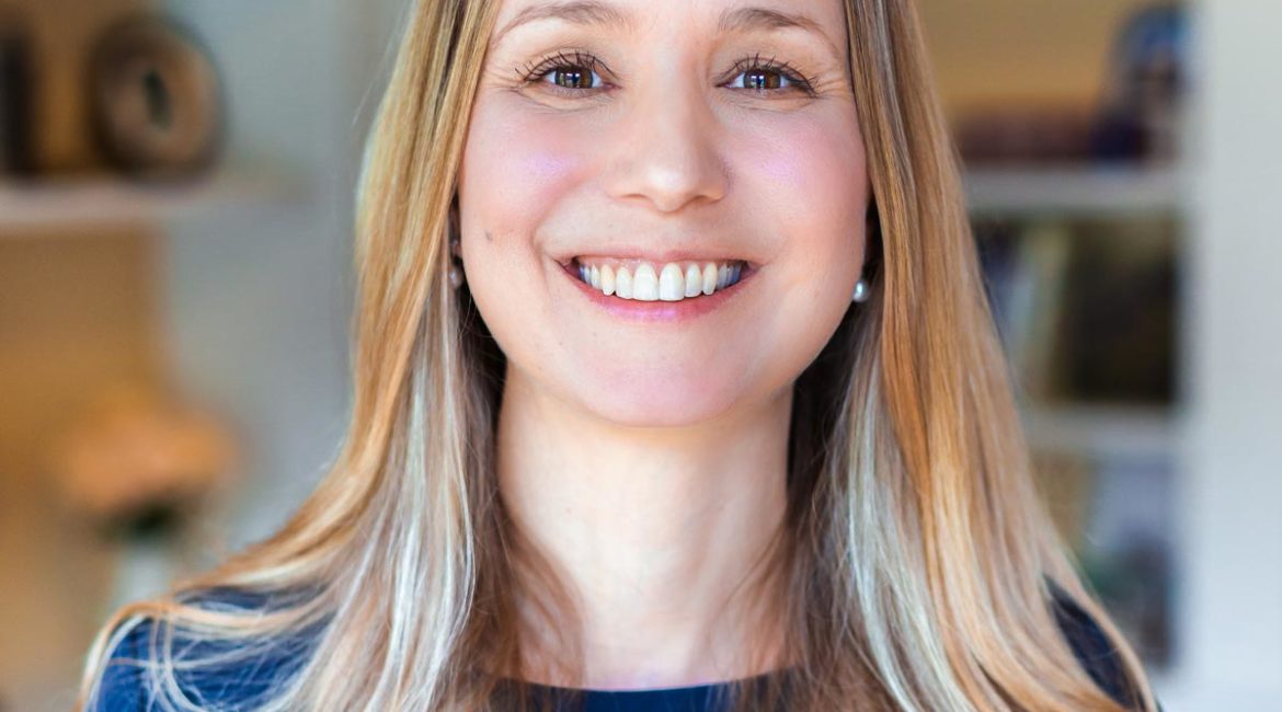 A woman smiling in front of a bookshelf.