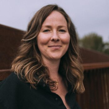 A woman in a black shirt standing next to a fence.