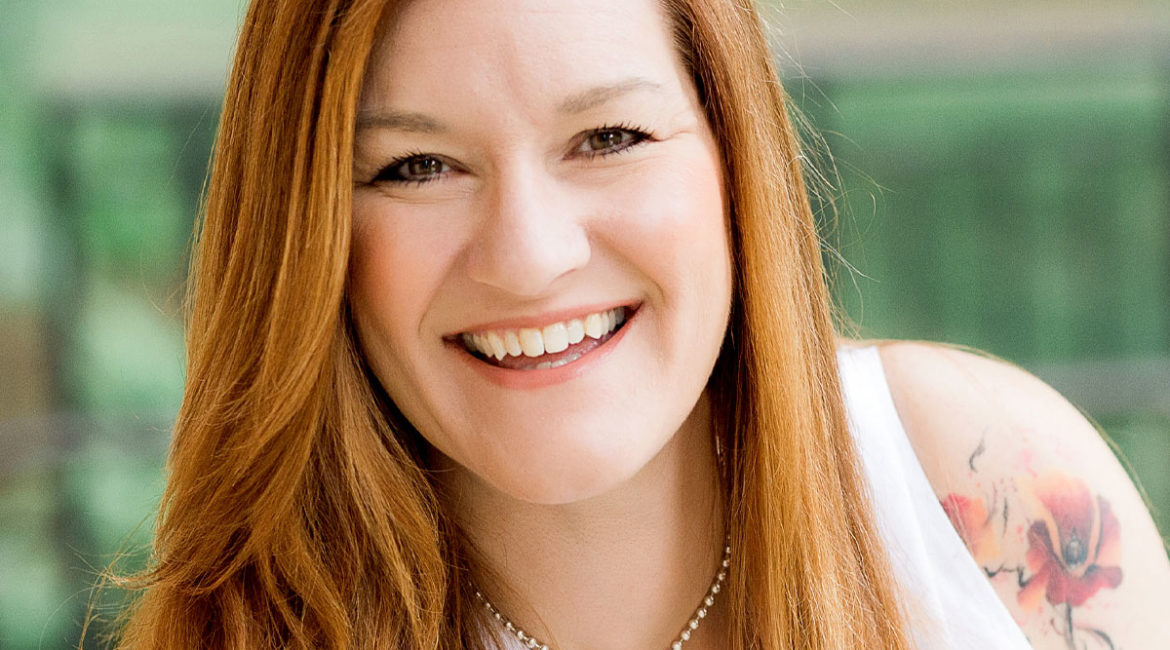 A smiling woman with red hair and tattoos.