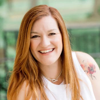 A smiling woman with red hair and tattoos.