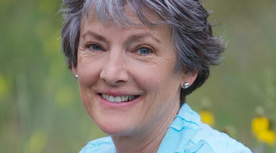 A woman with gray hair smiling in a field.