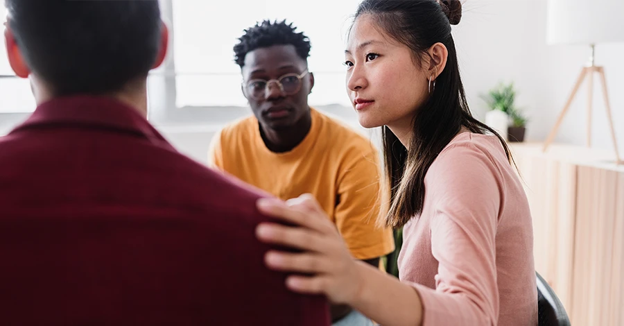Trauma Solutions: A woman places a supportive hand on the shoulder of a man, while another man looks on.