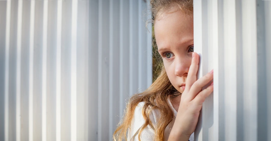 Trauma Solutions: A young girl looking to the side from behind a white vertical pillar.