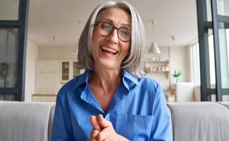 An older woman is participating in an Attachment and Trauma Mastery Program, sitting on a couch and smiling.