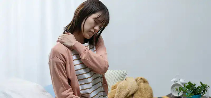 A woman reaches to comfort her own experience of chronic pain or tension. Muscle tension and chronic bracing are just one somatic symptom of unprocessed grief.