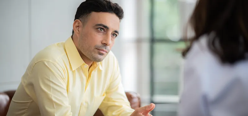 A therapist in a yellow shirt listens attentively to a client during a session, reflecting curiosity and attunement—modeling how clinicians can spot the subtle signs of encapsulated anxiety and trauma-related nervous system responses.