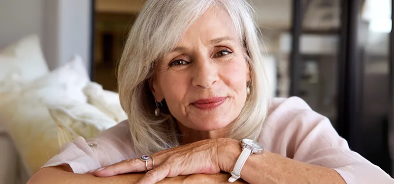 An older woman with gray hair smiles gently, resting her arms on a couch. Her calm and grounded expression conveys resilience, integration, and post-traumatic growth—capturing the healing potential when encapsulated anxiety is addressed with trauma-informed care.