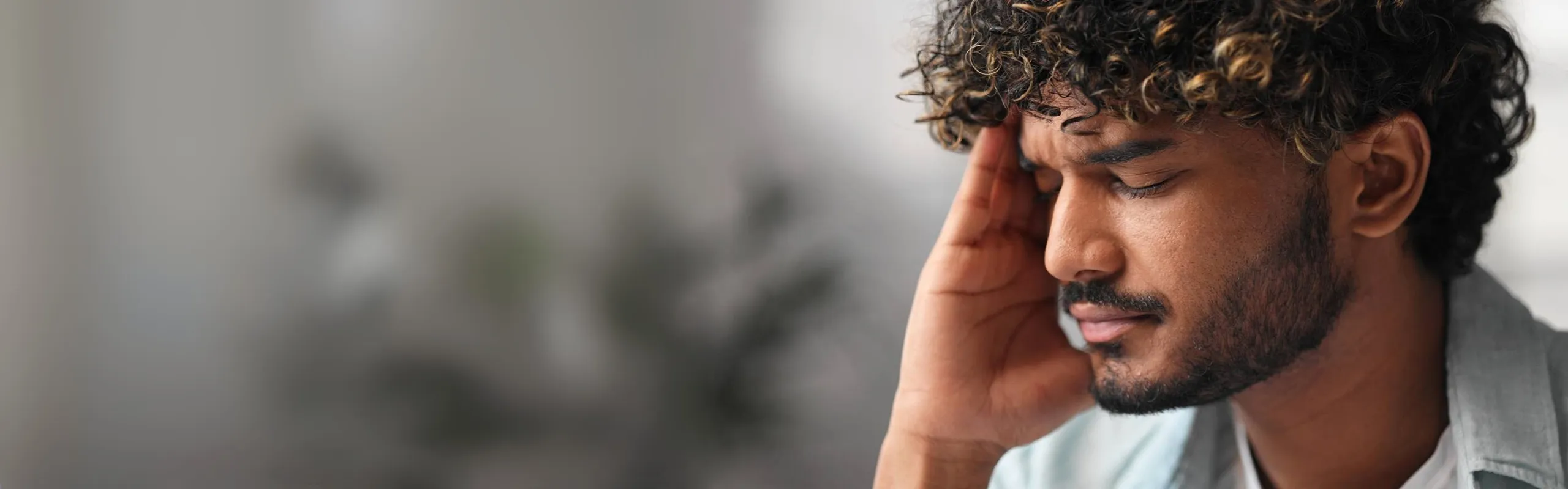 A young man with a pained expression holds his head, eyes closed in distress—illustrating the emotional and physiological toll of trauma-related anxiety and the unseen impact of encapsulated trauma on the nervous system.