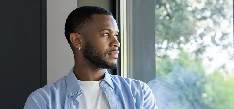 Trauma Solutions: A young man gazes from a window, appearing content and grounded in the present. Finding internal safety can allow disorganized adaptations to soften the need for protection.