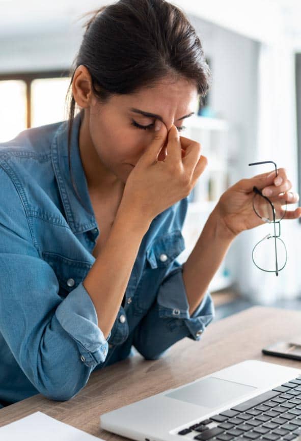 A woman is sneezing while working from home on her laptop.