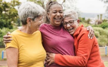 Three older women embracing in a park.