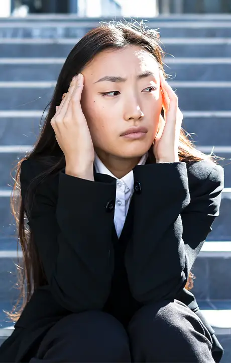 Trauma Solutions: A person in a black suit sits on outdoor steps, holding their head with both hands and looking to the side with a concerned expression.