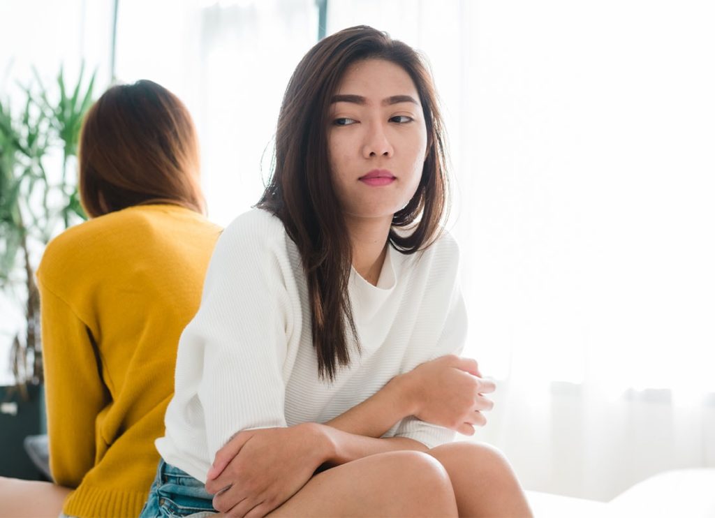 Two asian women sitting on a bed in front of a laptop.