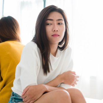 Two asian women sitting on a bed in front of a laptop.