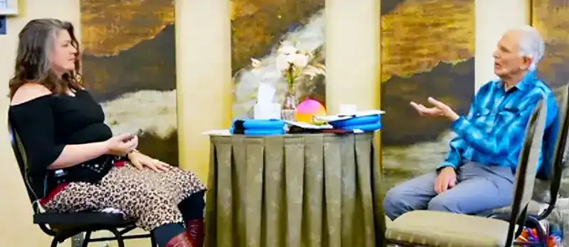 Trauma Solutions: Two people sit facing each other across a small round table in a room, appearing to be engaged in a conversation or interview.