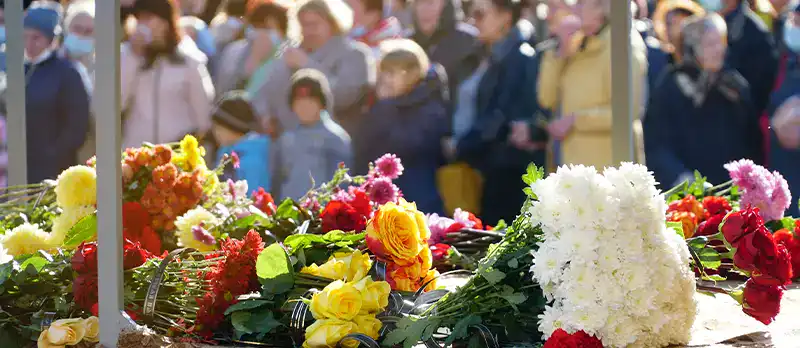 Trauma Solutions: Colorful flowers laid on a table in the foreground with a crowd of people standing and watching in the blurred background.