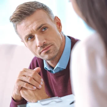 Trauma Solutions: A man in a sweater sitting and listening attentively to a woman off-camera.