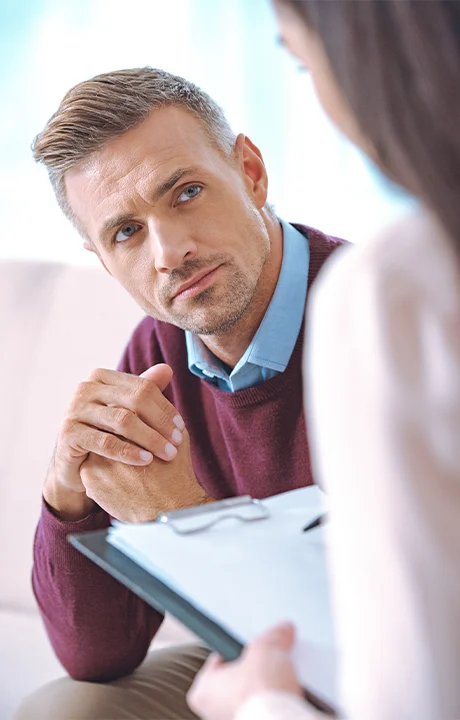 Trauma Solutions: A man sitting with his hands clasped, looking at someone holding a clipboard.